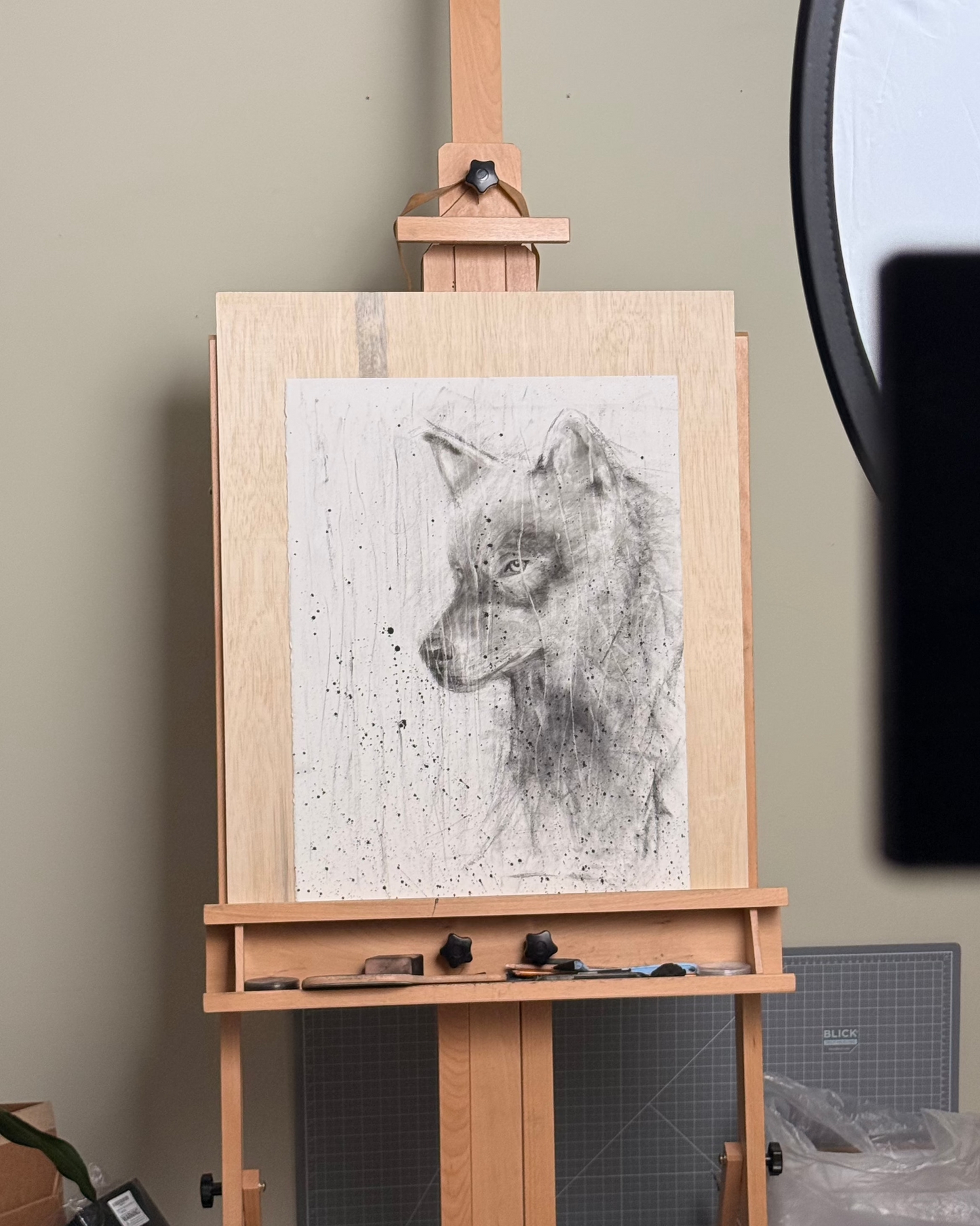 Wooden easel with a wolf portrait drawing on a gray wall background